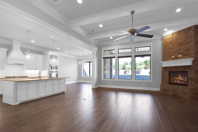 unfurnished living room featuring sink, a fireplace, ceiling fan, beamed ceiling, and dark hardwood / wood-style floors