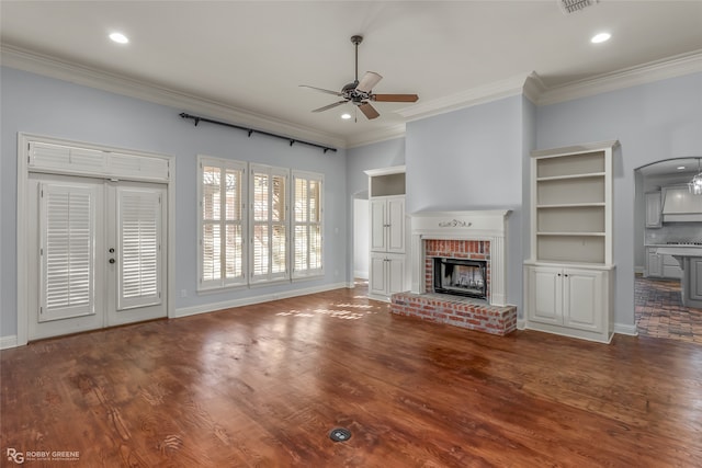 unfurnished living room featuring crown molding, ceiling fan, dark wood-type flooring, and a brick fireplace