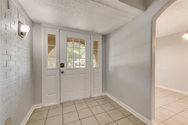 tiled foyer entrance featuring a textured ceiling and brick wall