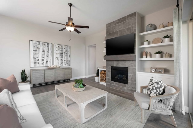 living room with ceiling fan, built in features, wood-type flooring, and a tile fireplace