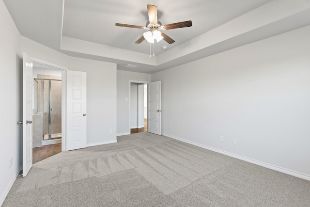 unfurnished bedroom featuring light carpet, connected bathroom, a tray ceiling, and ceiling fan