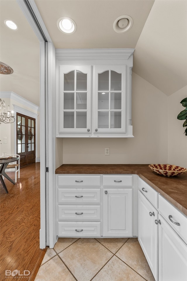 kitchen with light wood-type flooring, french doors, lofted ceiling, white cabinets, and an inviting chandelier