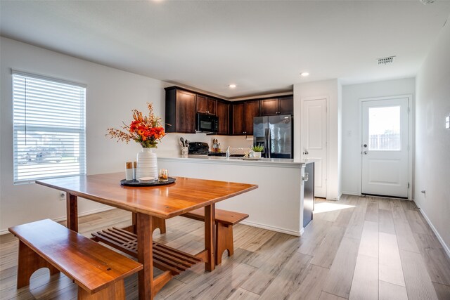 kitchen with stove, kitchen peninsula, dark brown cabinets, light wood-type flooring, and stainless steel fridge