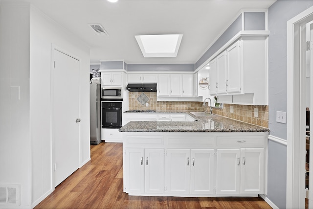 kitchen featuring dark stone counters, stainless steel appliances, sink, hardwood / wood-style flooring, and white cabinets