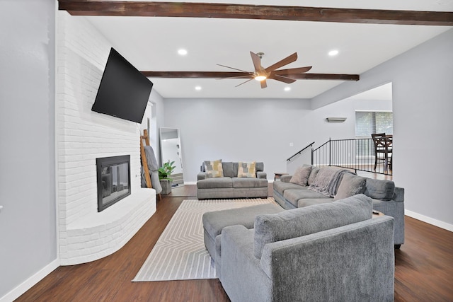 living room featuring beam ceiling, ceiling fan, dark wood-type flooring, and a brick fireplace