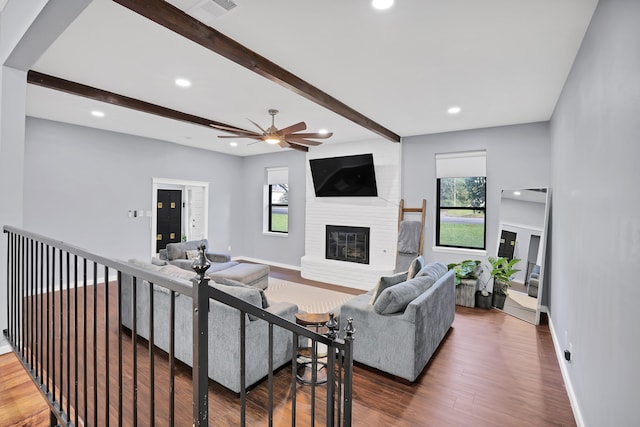 living room with a large fireplace, ceiling fan, dark hardwood / wood-style flooring, and beam ceiling