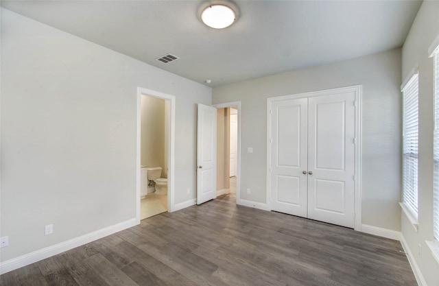 unfurnished bedroom featuring dark hardwood / wood-style floors, a closet, and ensuite bath