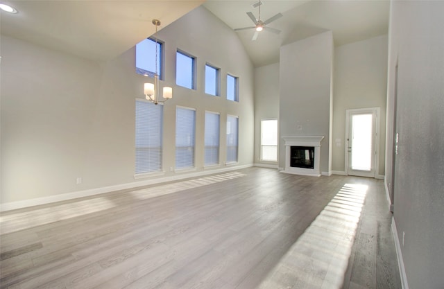 unfurnished living room featuring ceiling fan with notable chandelier, a towering ceiling, and light hardwood / wood-style flooring