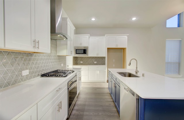 kitchen featuring white cabinets, appliances with stainless steel finishes, wall chimney exhaust hood, an island with sink, and sink