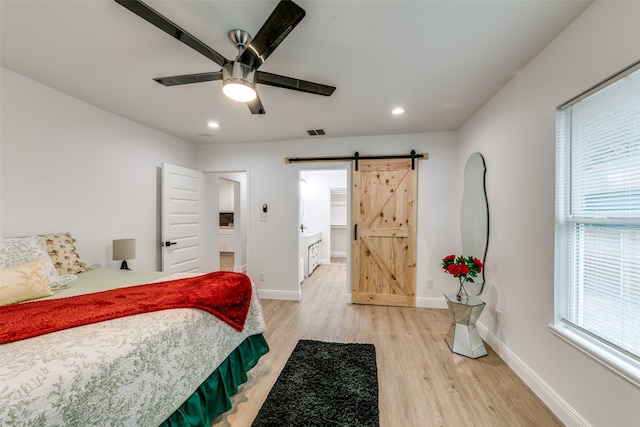 bedroom with connected bathroom, a barn door, hardwood / wood-style flooring, and ceiling fan