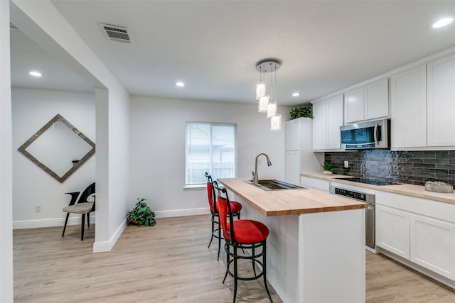 kitchen featuring a center island with sink, appliances with stainless steel finishes, wood counters, white cabinetry, and sink