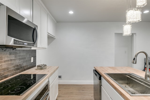 kitchen featuring appliances with stainless steel finishes, butcher block counters, hanging light fixtures, and white cabinetry