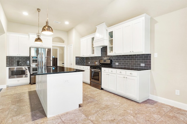 kitchen with a kitchen island with sink, white cabinetry, stainless steel appliances, decorative backsplash, and decorative light fixtures