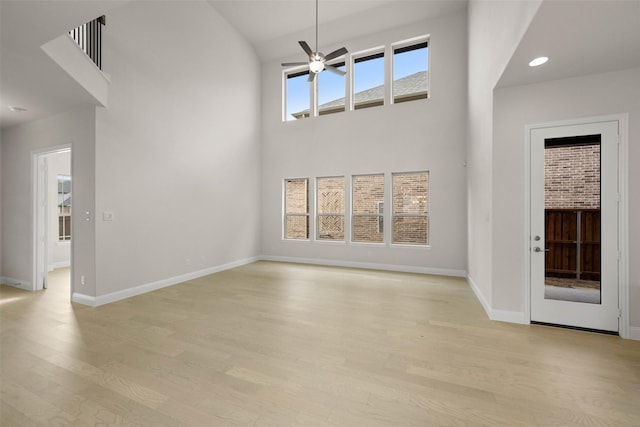 unfurnished living room with light hardwood / wood-style floors, ceiling fan, and a high ceiling