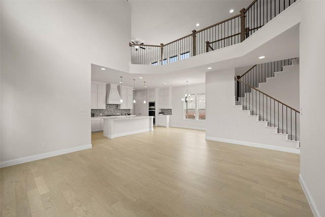 unfurnished living room featuring a towering ceiling, ceiling fan with notable chandelier, and light wood-type flooring