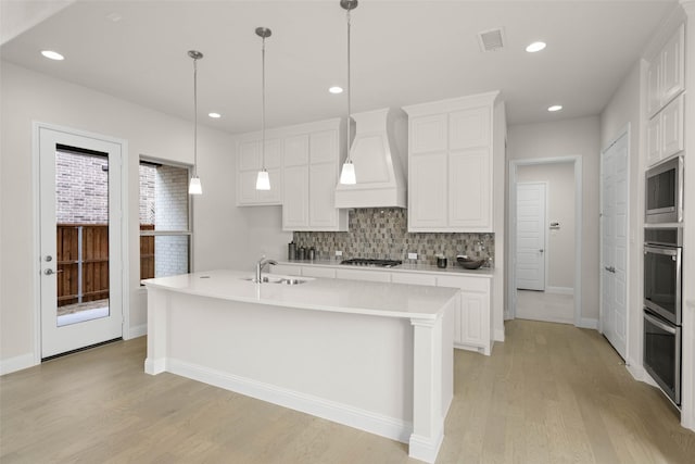 kitchen featuring stainless steel appliances, white cabinetry, custom range hood, and a kitchen island with sink