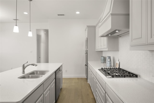 kitchen with stainless steel appliances, a sink, light wood-type flooring, backsplash, and custom range hood