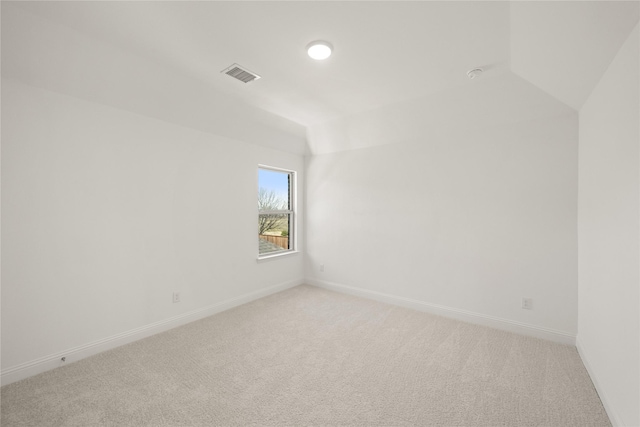 spare room featuring light carpet, vaulted ceiling, visible vents, and baseboards