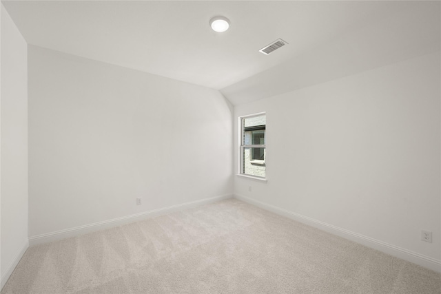 spare room with light carpet, baseboards, visible vents, and lofted ceiling