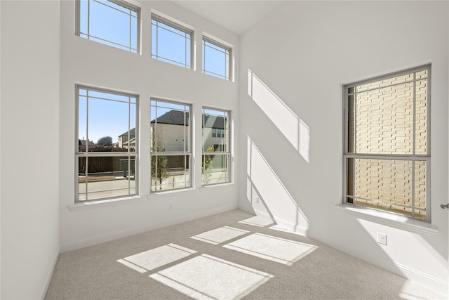 carpeted empty room with a towering ceiling and baseboards