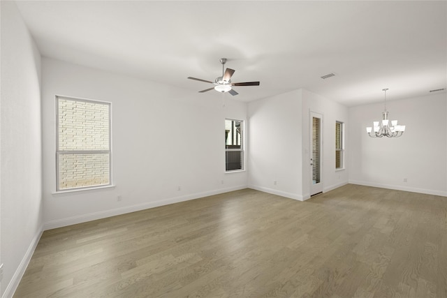 empty room featuring ceiling fan with notable chandelier, light wood finished floors, visible vents, and baseboards