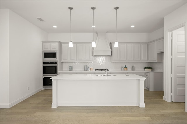 kitchen featuring double oven, light wood-type flooring, black microwave, and custom exhaust hood