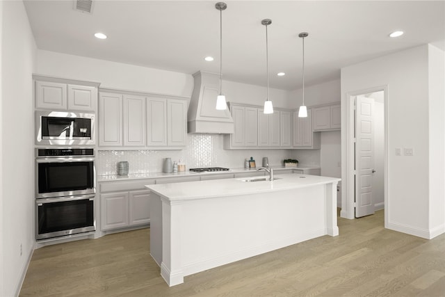 kitchen with light wood finished floors, stainless steel appliances, light countertops, a sink, and premium range hood