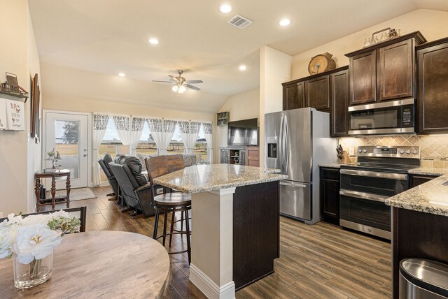 kitchen with a kitchen island, light stone counters, stainless steel appliances, and dark hardwood / wood-style flooring