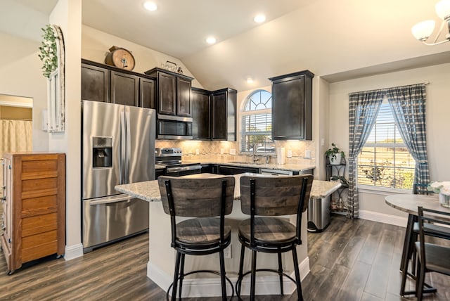 kitchen featuring dark hardwood / wood-style floors, vaulted ceiling, a center island, appliances with stainless steel finishes, and tasteful backsplash