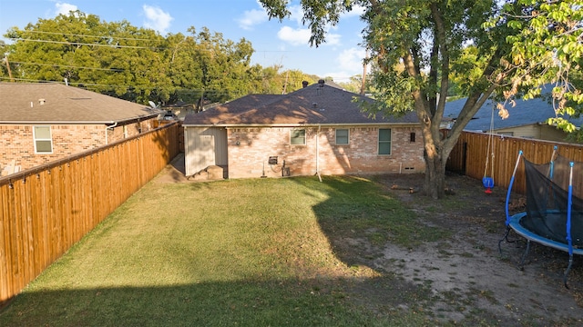 rear view of property featuring a trampoline and a lawn