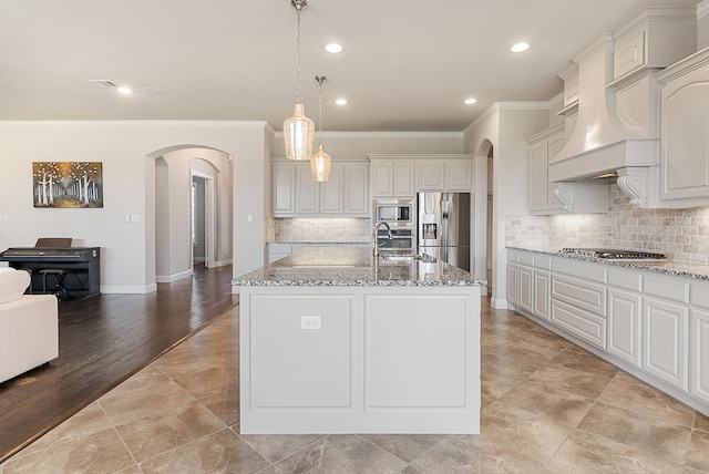 kitchen with sink, hanging light fixtures, appliances with stainless steel finishes, an island with sink, and light stone countertops