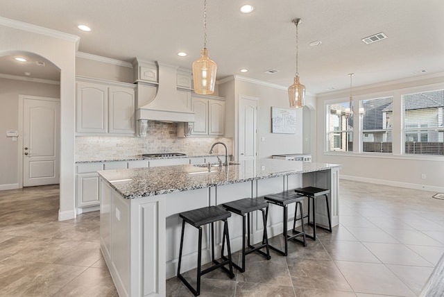 kitchen with decorative light fixtures, white cabinets, custom range hood, and a center island with sink