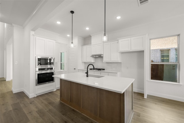 kitchen with pendant lighting, white cabinets, dark hardwood / wood-style flooring, stainless steel appliances, and a center island with sink