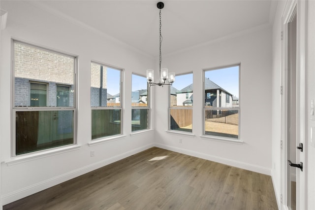 unfurnished dining area featuring hardwood / wood-style floors, crown molding, and an inviting chandelier