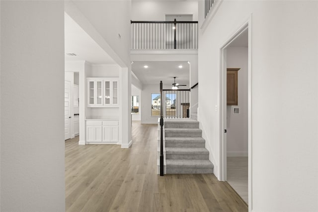 foyer entrance featuring light wood-type flooring, ceiling fan, and a towering ceiling