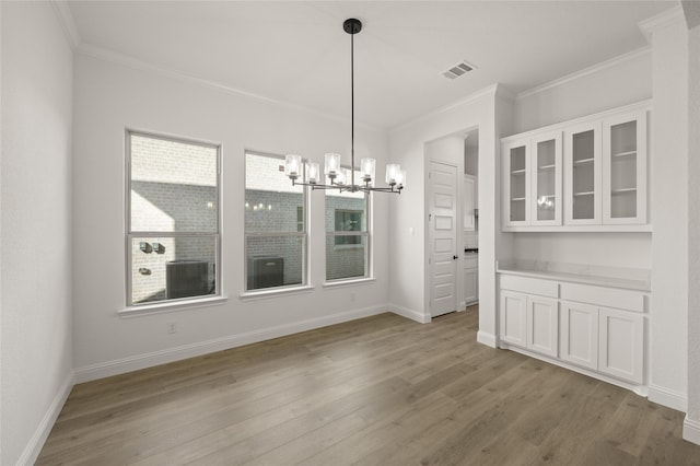 unfurnished dining area with crown molding, light hardwood / wood-style floors, and a notable chandelier