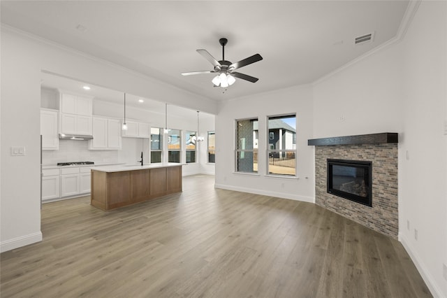 kitchen with white cabinetry, a stone fireplace, an island with sink, gas stovetop, and hanging light fixtures