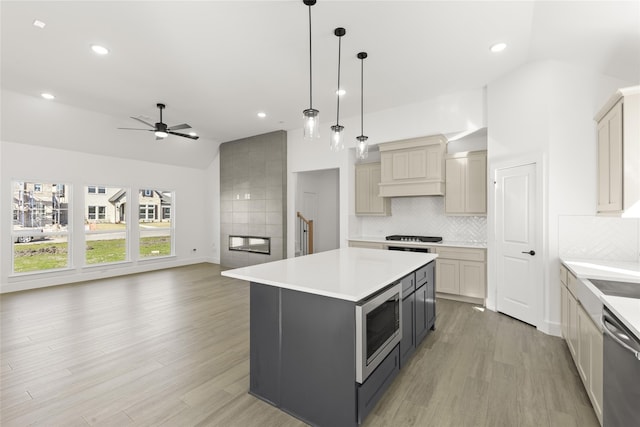 kitchen with light wood finished floors, tasteful backsplash, appliances with stainless steel finishes, vaulted ceiling, and light countertops
