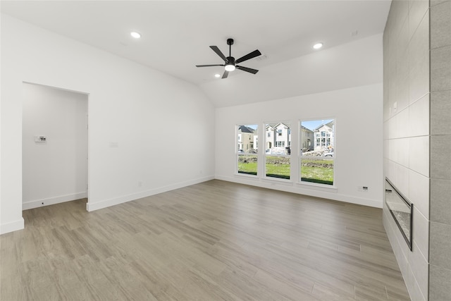 unfurnished living room with vaulted ceiling, a tile fireplace, a ceiling fan, and light wood-style floors