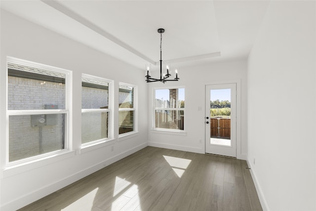 unfurnished dining area featuring a notable chandelier, a tray ceiling, wood finished floors, and baseboards