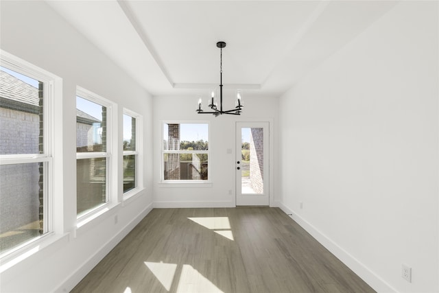 unfurnished dining area with an inviting chandelier, baseboards, a raised ceiling, and wood finished floors