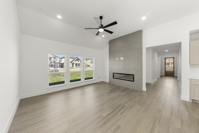 unfurnished living room with lofted ceiling, a ceiling fan, light wood-type flooring, baseboards, and a tile fireplace
