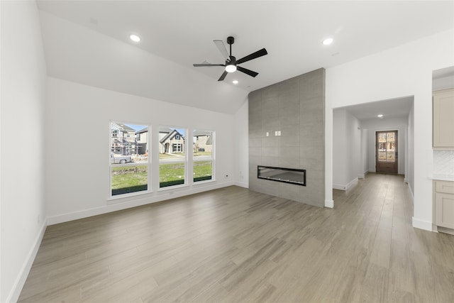 unfurnished living room featuring light wood finished floors, baseboards, a tiled fireplace, ceiling fan, and vaulted ceiling