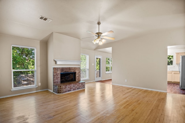 unfurnished living room with light hardwood / wood-style flooring, a brick fireplace, a healthy amount of sunlight, and ceiling fan