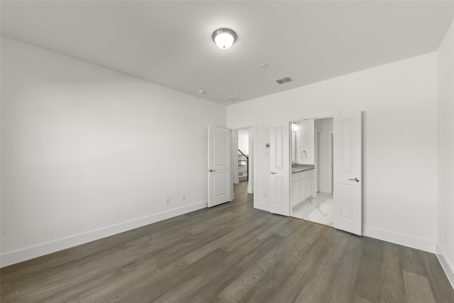 unfurnished bedroom featuring ensuite bathroom and dark wood-type flooring