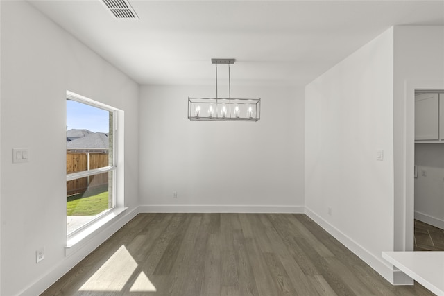 unfurnished dining area featuring a chandelier, a healthy amount of sunlight, and dark hardwood / wood-style floors