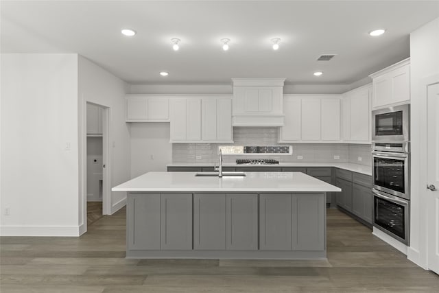 kitchen featuring sink, dark hardwood / wood-style floors, backsplash, gray cabinets, and a kitchen island with sink