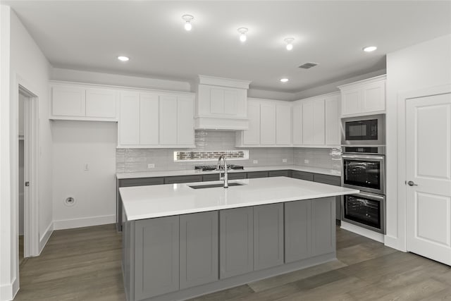 kitchen with white cabinets, a kitchen island with sink, oven, and black microwave