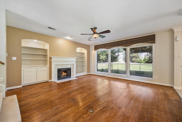 unfurnished living room with hardwood / wood-style floors, a tiled fireplace, built in features, and ceiling fan