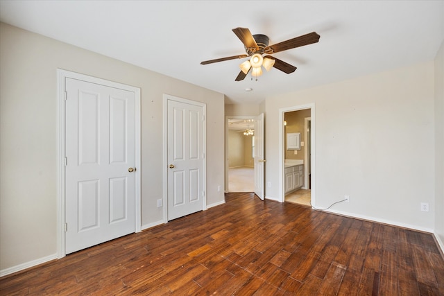 unfurnished bedroom with multiple closets, ensuite bathroom, dark wood-type flooring, and ceiling fan